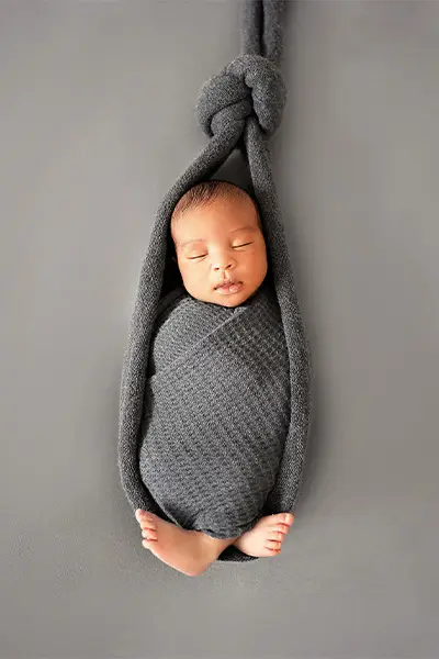 Newborn baby wrapped snugly in a gray sling, suspended against a gray background, peacefully sleeping, photographed by Dia Kiss, a Chicago suburbs photographer.