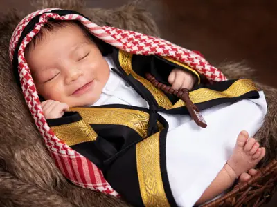 A smiling baby dressed in traditional Aramaic attire, photographed in a warm studio setting.