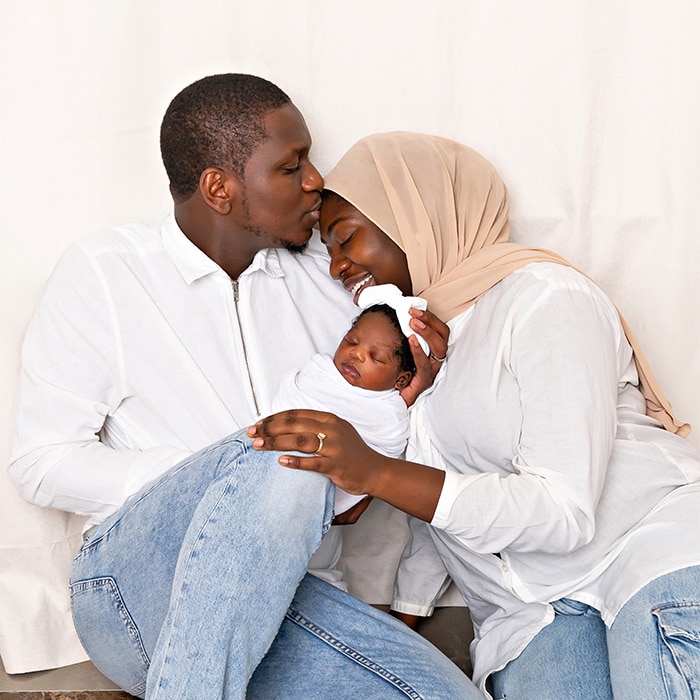 Naperville newborn photography by Dia Kiss, showing a family embracing their newborn, with the father kissing the mother as she holds the baby.