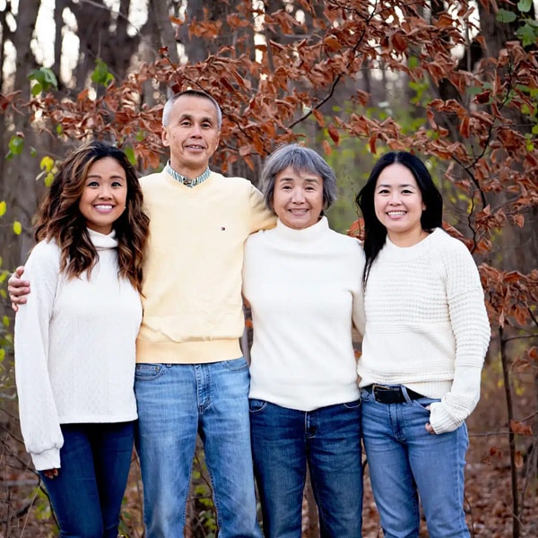 A family of four posing together in an autumn forest with colorful leaves and trees in the background.