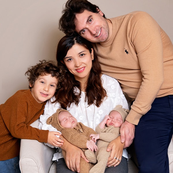 A family portrait featuring parents, an older sibling, and newborn twins dressed in cozy knit outfits.