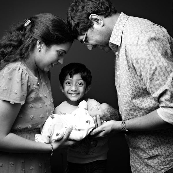 A family of four with parents and a young child admiring their newborn baby in a touching portrait.