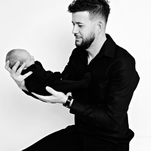 A father holding and admiring his newborn baby in a black-and-white studio setting.