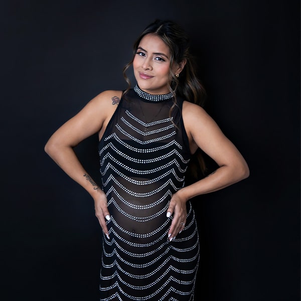 A pregnant woman in a patterned black dress, confidently posing against a black background