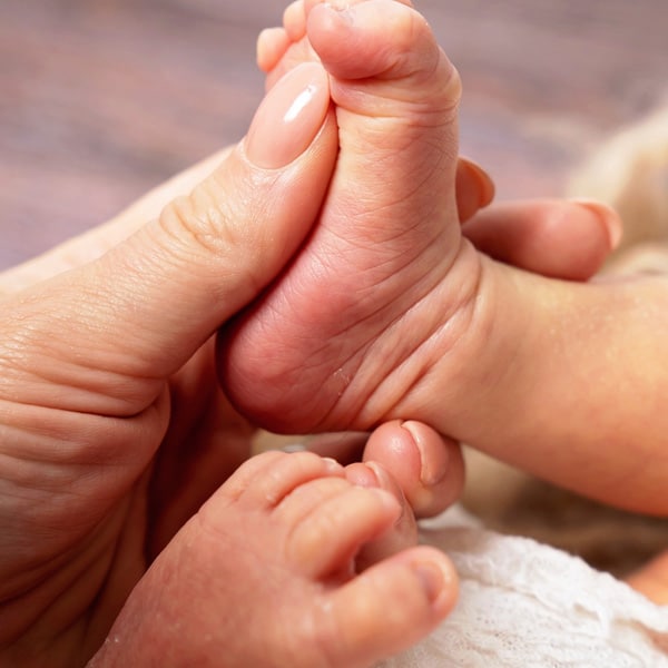 A close-up of a parent gently holding a newborn baby's tiny feet, resting on a soft background.