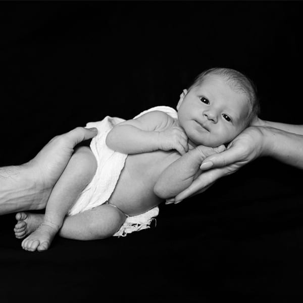 A newborn baby gently supported by their parents' hands, resting on a dark background.