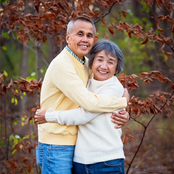 A smiling senior couple embracing in an outdoor setting with autumn leaves and trees in the background.